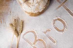Ein mit Mehl bestreuter Holztisch, auf dem einige Getreideähren und ein Brot liegen. In das Mehl wurde "Brot" geschrieben.