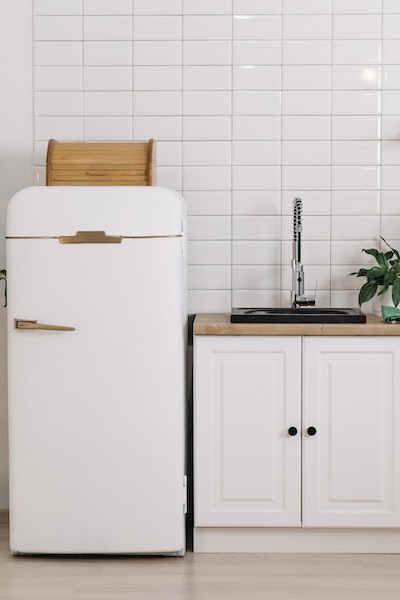 Neben einer weißen Küchenzeile steht ein Kühlschrank im Retro-Look, auf ihm ein hölzerner Brotkasten