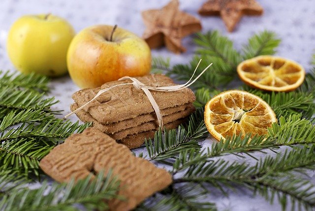 Auf einigen Tannenzweigen, neben getrockneten Orangenscheiben und einigen Äpfeln liegen Spekulatius-Kekse.