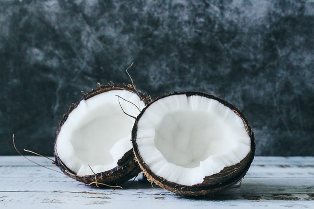 Eine halbierte Kokosnuss liegt mit dem weißen Fruchtfleisch nach oben auf einer hellen Holzfläche