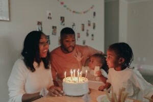 Um einen gedeckten Tisch sitzt eine Familie mit zwei Kindern, in der Mitte steht ein Geburtstagskuchen