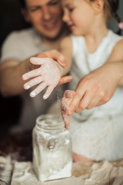 Ein Mann hilft einem Kind dabei, sich die Hände voller Mehl abzustauben