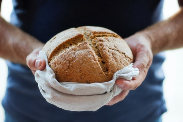 Jemand hält ein Brot mit einem Handtuch in seinen Händen. Es ist kreuzförmig eingeschnitten.