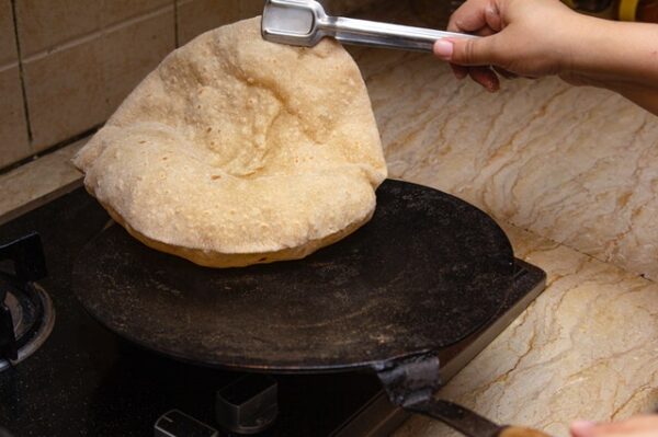 Eine Person hält mit einer Zange ein Naan Brot über eine heiße Platte.
