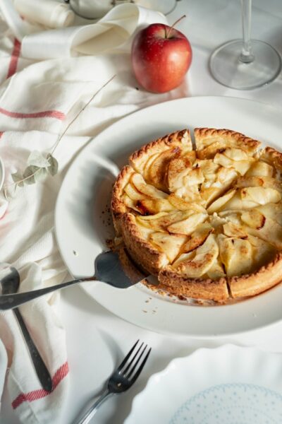 Auf einem weißen Teller steht ein in Stücke geteilter Apfelkuchen
