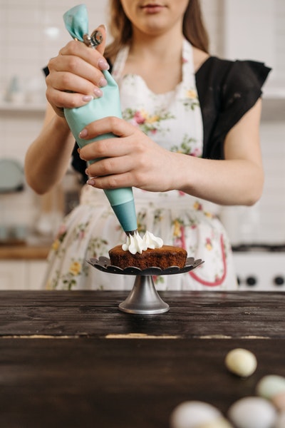 Eine Frau setzt mit einer Spritztülle Sahnetupfen auf einen Kuchen