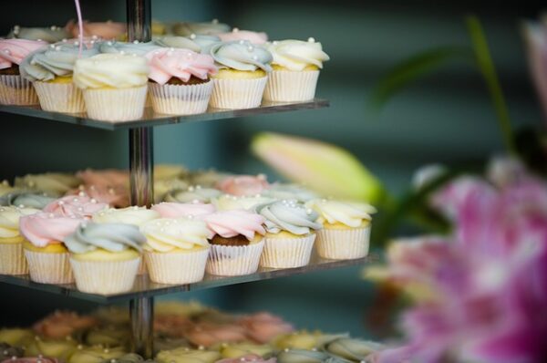 Auf einer mehrstöckigen Glasetagere stehen verschiedene kleine, pastellfarbige, mit Perlen verzierte Cupcakes 