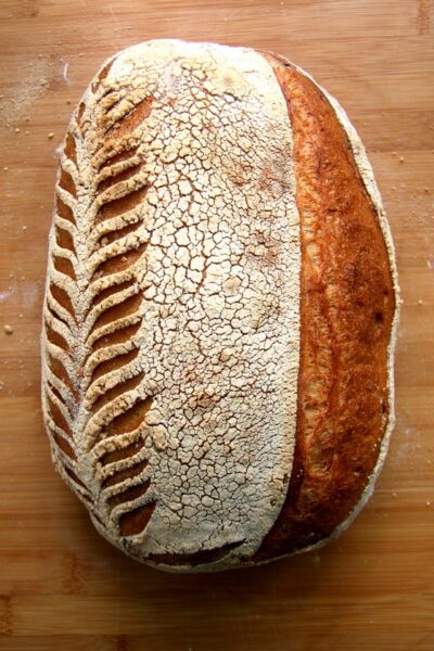 Ein länglich geformtes Brot mit seitlichen Einschnitten liegt auf einem Holztisch