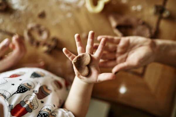 Eine Kinderhand hält ein aus Teig geformtes Herz. Die Hand einer erwachsenen Person ist darunter