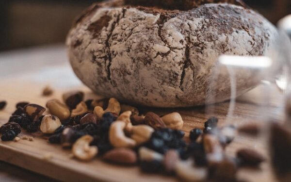 Ein rundes Brot mit Bemehlung liegt auf einem Holzbrett, drumherum verschiedene Nüsse