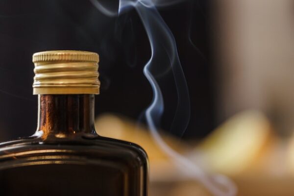 Das obere Ende einer braunen Flasche mit Schraubverschluss, daneben steigt dünn Rauch auf