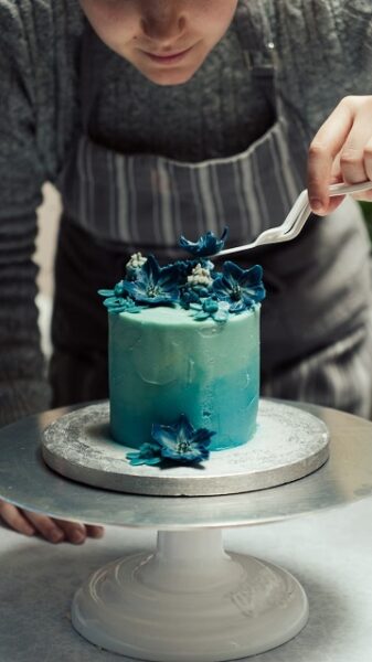 Eine Person platziert blaue Blüten auf einem blau eingedeckten Kuchen