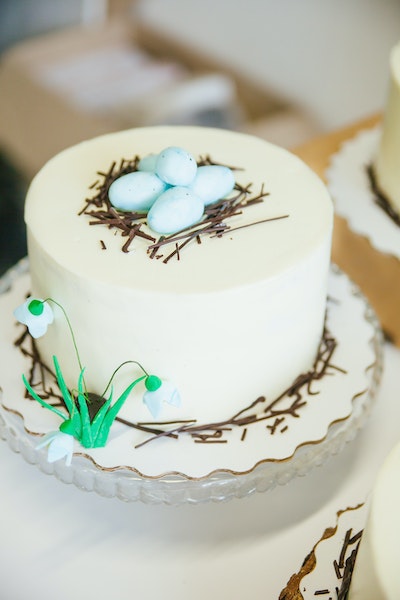 Eine mit weißem Fondant eingedeckte Torte samt Ostereiern und Schneeglöckchen als Dekoration steht auf einer Kuchenplatte