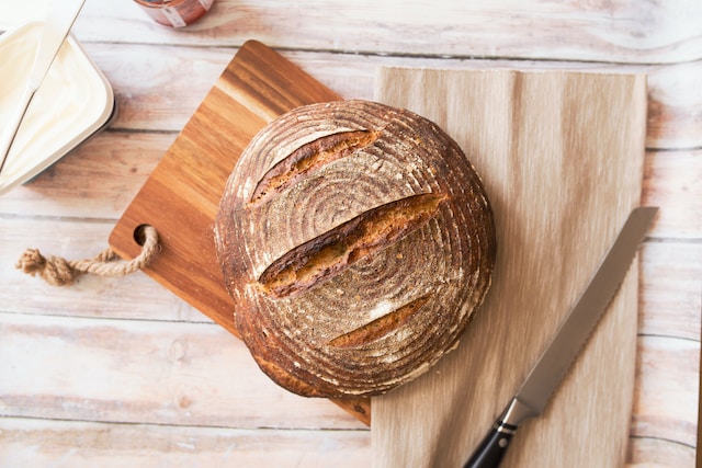 ein frisch gebackenes, rundes Brot liegt neben einem großen Messer auf einem Holzbrett