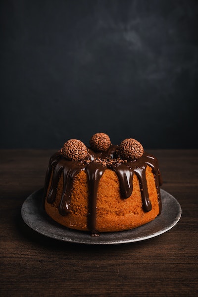 ein kleiner runder Kuchen steht auf einem Teller, er ist dekoriert mit Rumkugeln und von ihm tropft eine dicke Schicht Schokoglasur