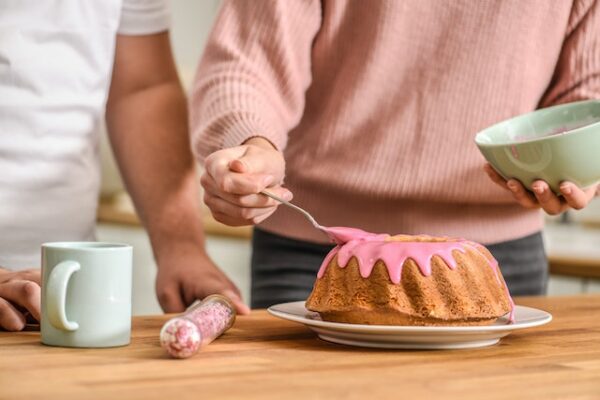 Jemand streicht rosafarbenen Zuckerguss über einen Kuchen